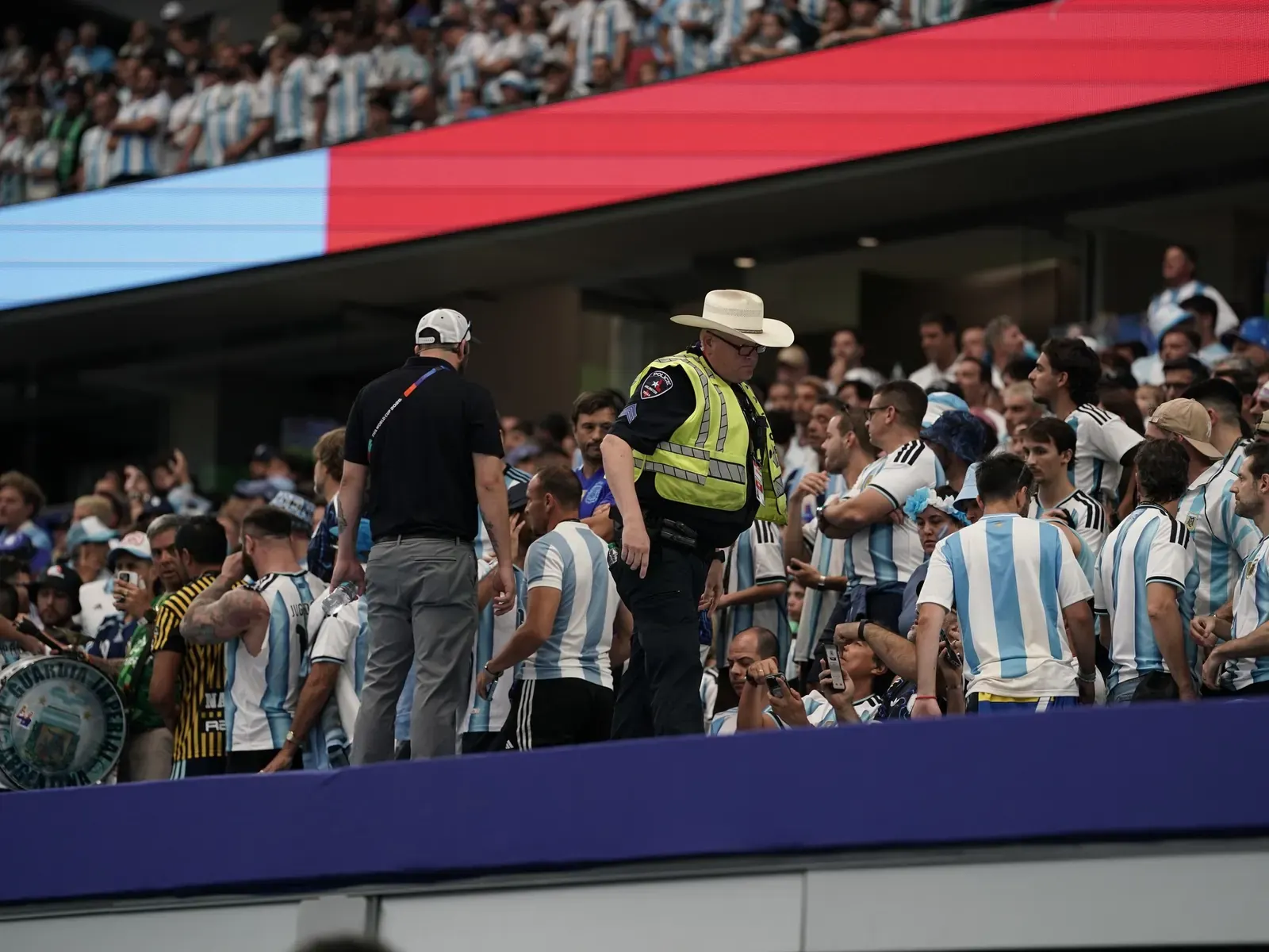 Imagen ilustrativa de hinchas argentinos en un evento deportivo, con el logo del Ministerio de Seguridad de Argentina al fondo.