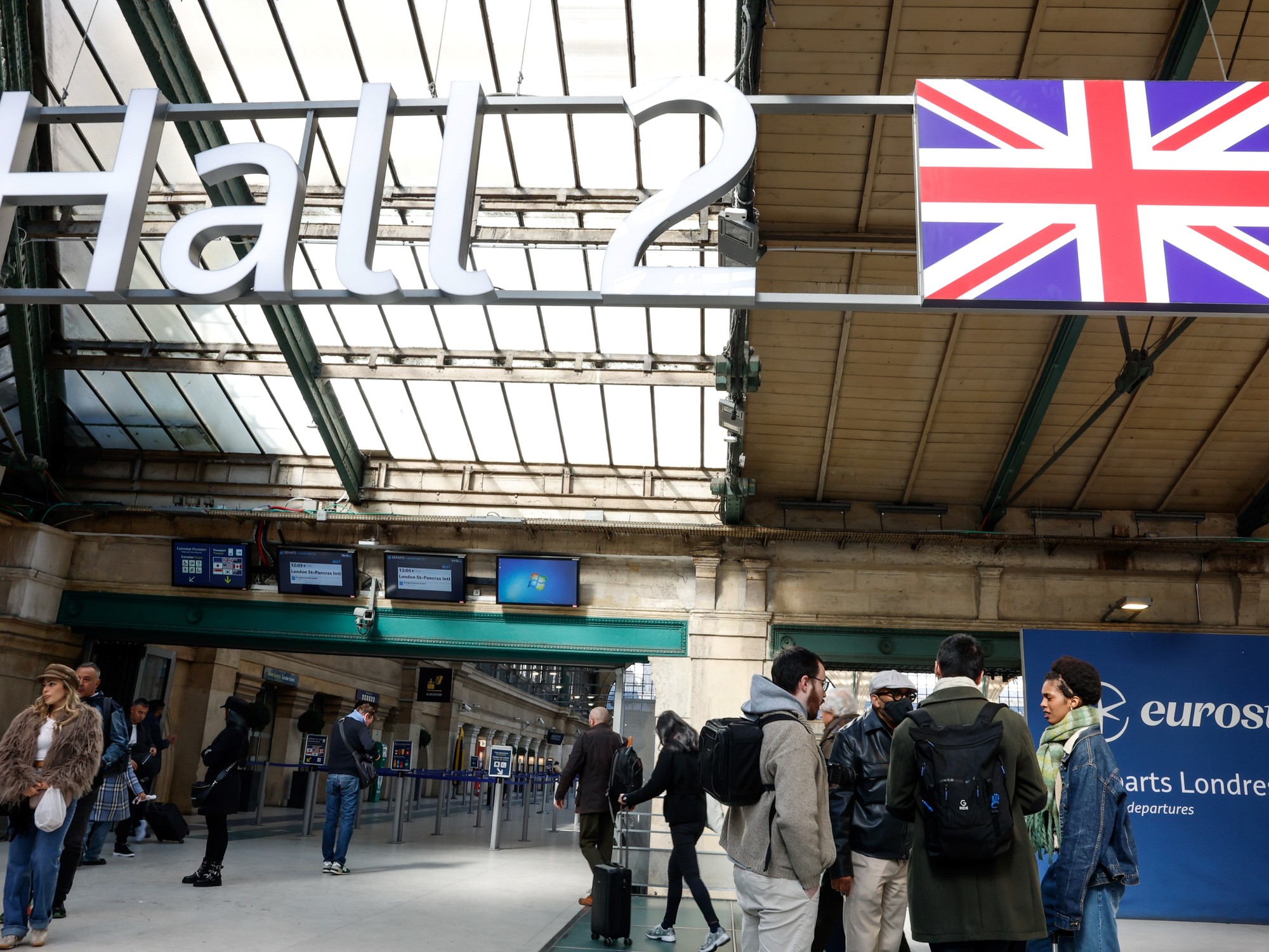 Turistas y pasajeros aguardan información en una terminal aeroportuaria internacional, con carteles indicando destinos a Londres, Reino Unido.