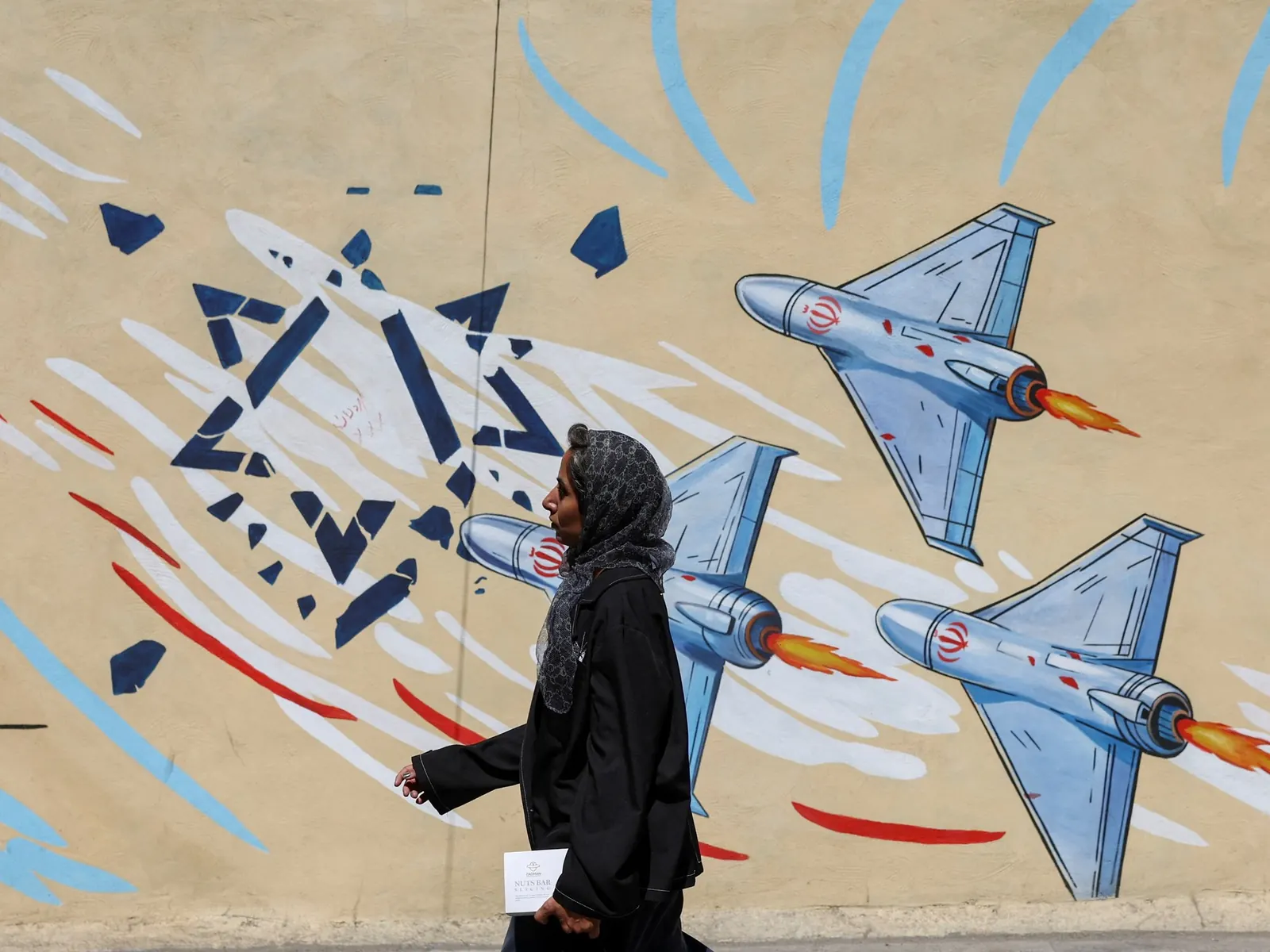 Mujer iraní caminando frente a un mural con consignas políticas en Teherán.
