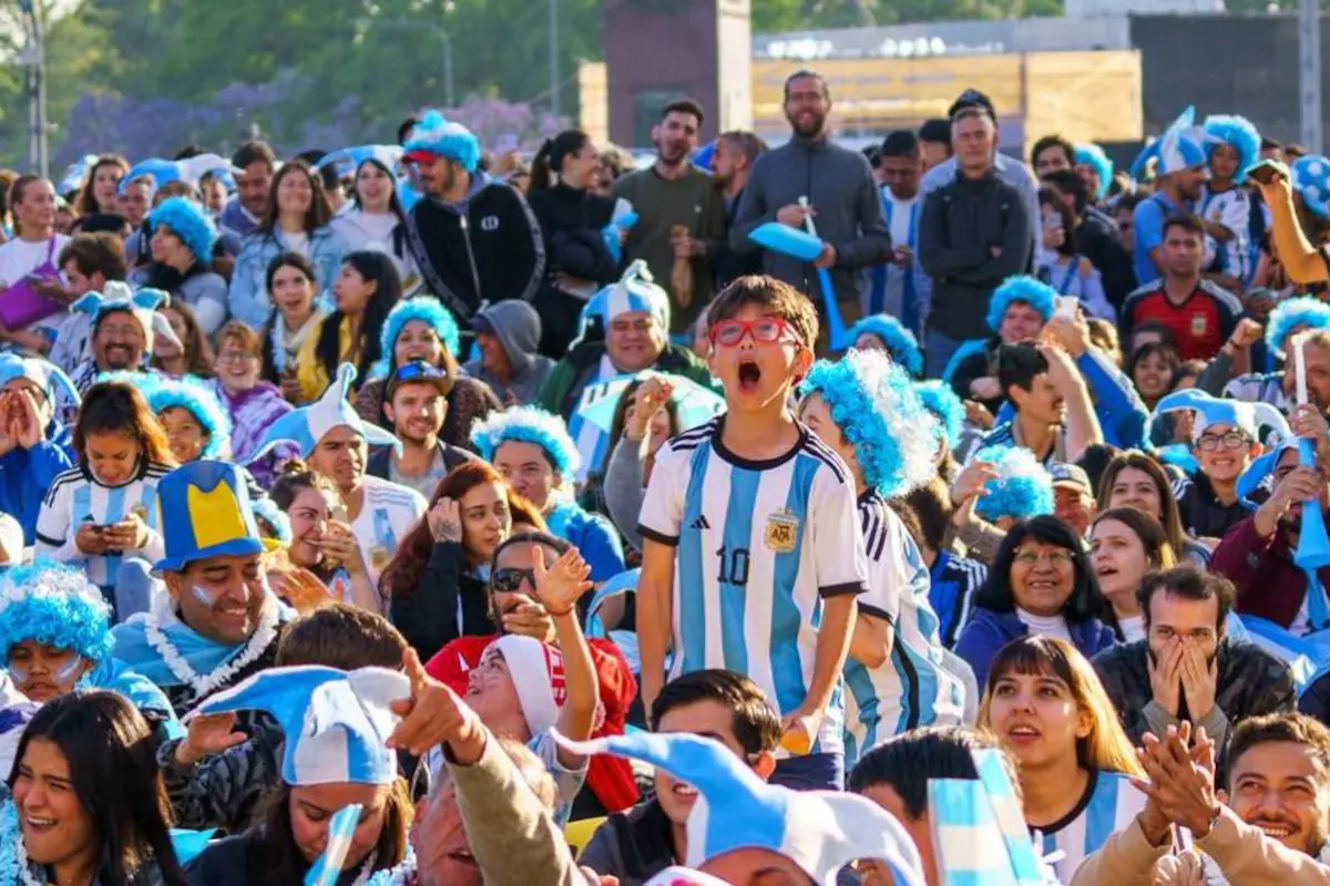 Hinchas argentinos celebrando con la bandera del país, un motorhome estacionado cerca de un estadio de fútbol.