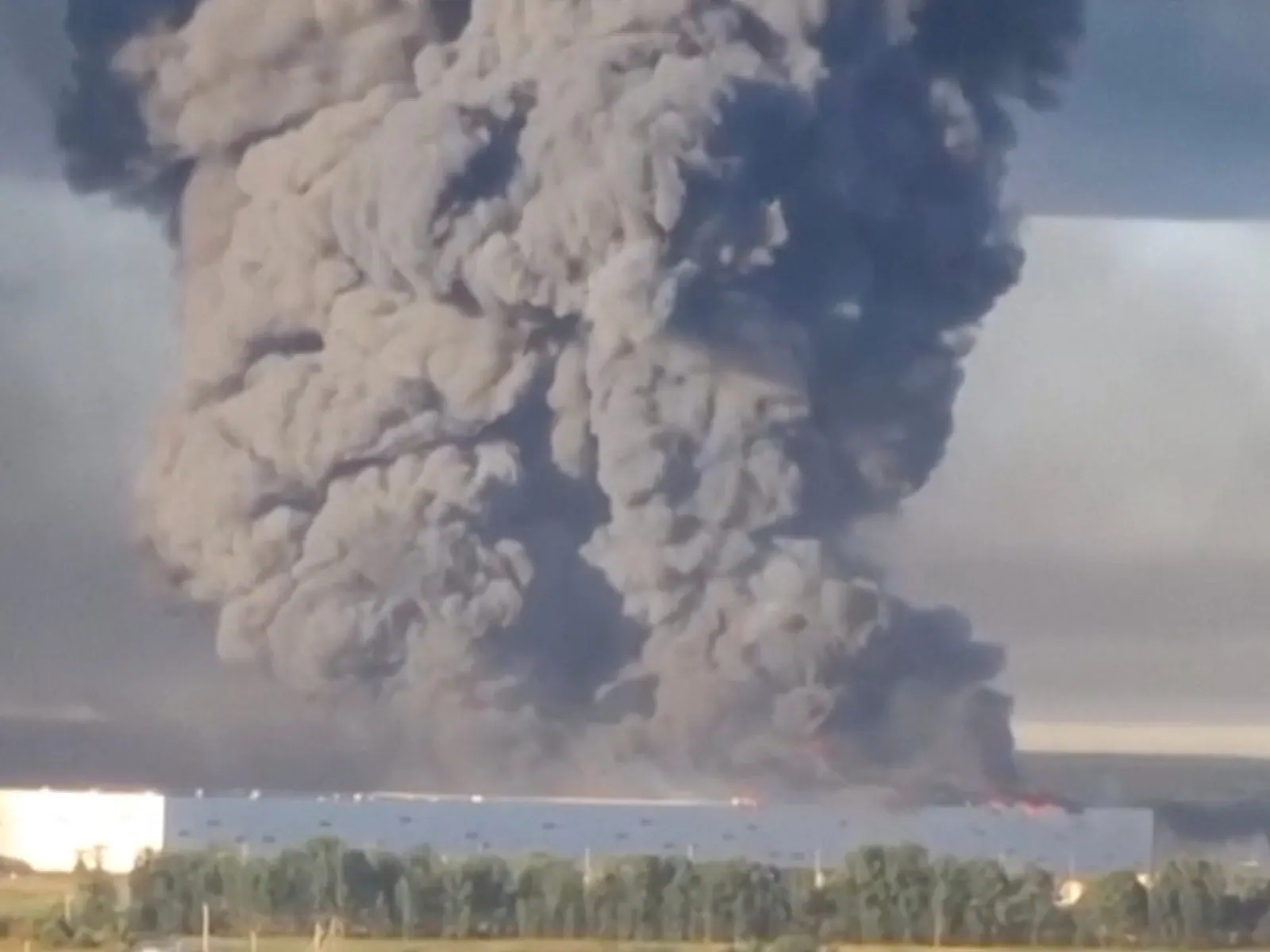 Vista aérea de un gran almacén de comercio electrónico en llamas, con columnas de humo negro elevándose hacia el cielo, tras un ataque con drones en Rusia.